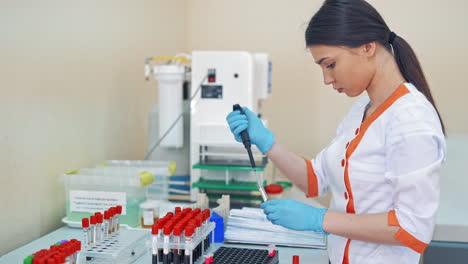 beautiful laboratory technician woman in medical uniform works with blood samples. female researcher is working with many vials of liquid in the laboratory.