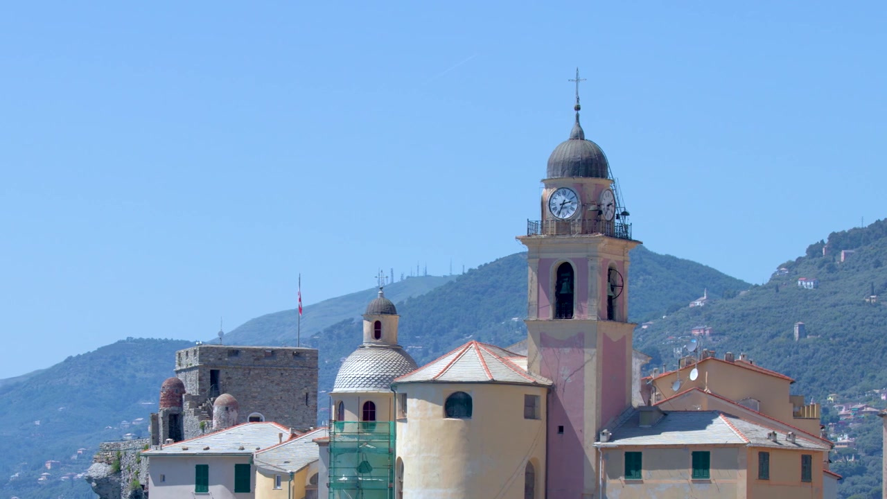 Inquadratura ampia statica di una torre di chiesa storica e di colorati edifici mediterranei su uno sfondo di colline verdi