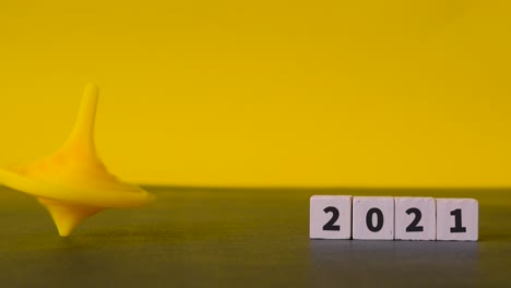 human hand spins a yellow top that wobbles and settles neatly next to wooden blocks with the numbers 2021 on them