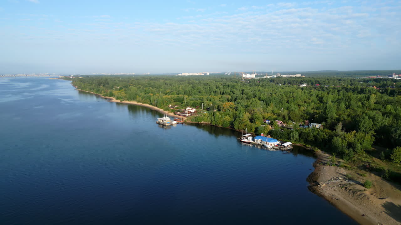 Aerial view of a wide river next to a lush forest and a distant city skyline