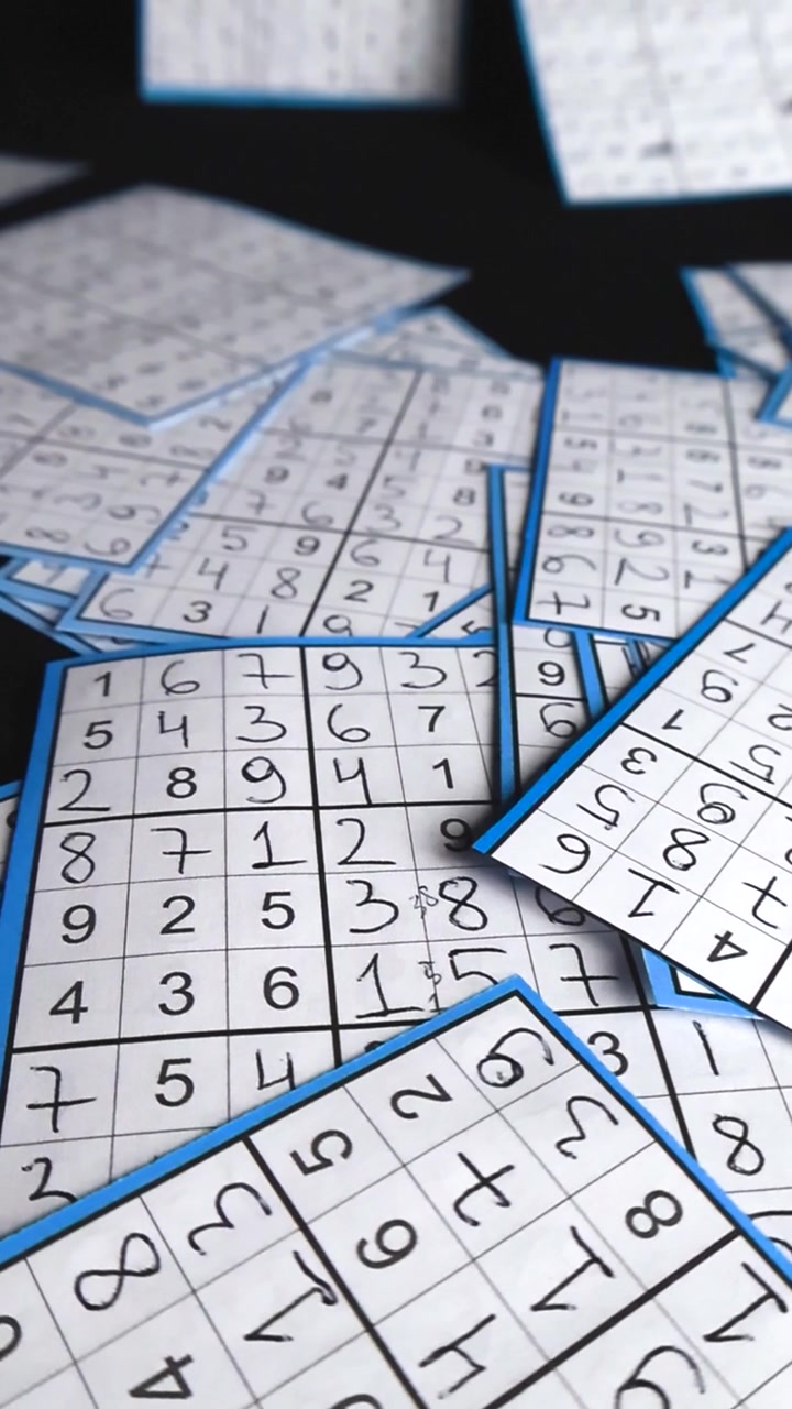 Vista aproximada de cartões de quebra-cabeça de sudoku resolvidos e escritos à mão, dispostos aleatoriamente sobre um fundo de estúdio preto, exibindo o conceito de lógica, resolução de problemas e desafios intelectuais
