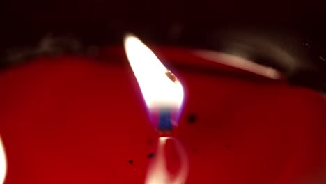 side angle view of candle wick burning slow, light reflection across red wax