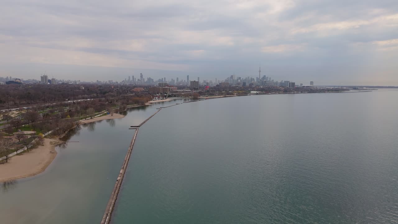 Breakwater structures by coast and distant Toronto skyline, wide aerial