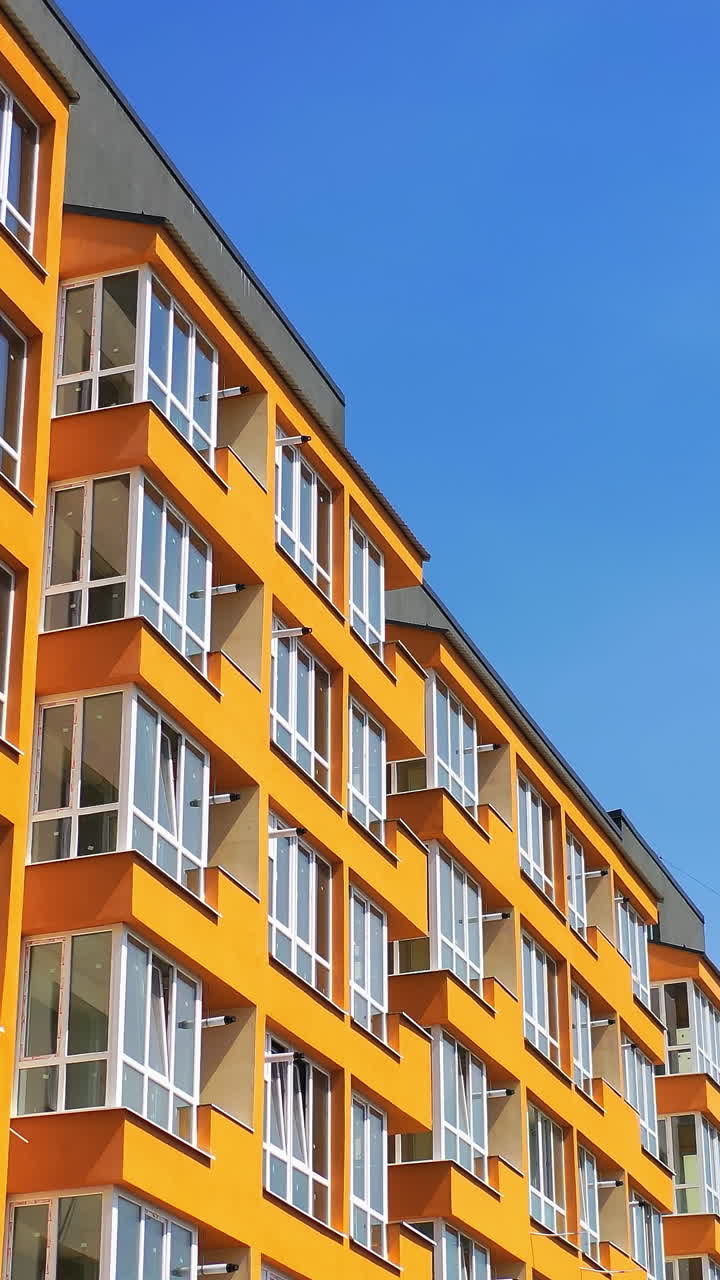 Bright city architecture against blue sky. New apartment building in orange color for urban residents. Modern design of high-rise building. Vertical video