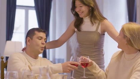 Happy-Parents-Sitting-At-Table-And-Clinking-Glasses-When-Pretty-Teenage-Daughter-Coming-Up-And-Hugging-And-Kissing-Them