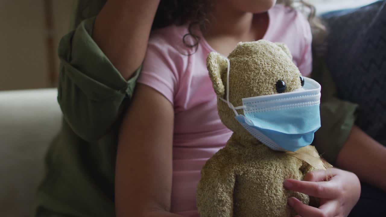 Mixed race mother and daughter hugging,daughter holding tedy bear with face mask