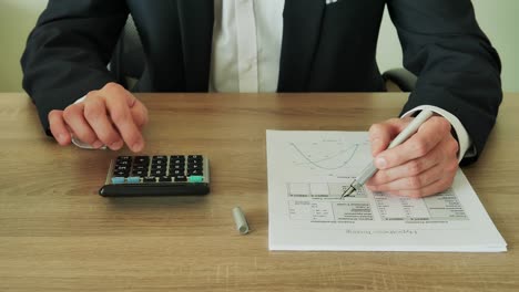 businessman checks the calculations on a calculator in the office of wooden table 4k