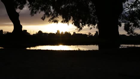 el sol se pone detrás de un paisaje urbano recortado, mientras una persona corre junto a un charco de agua en primer plano