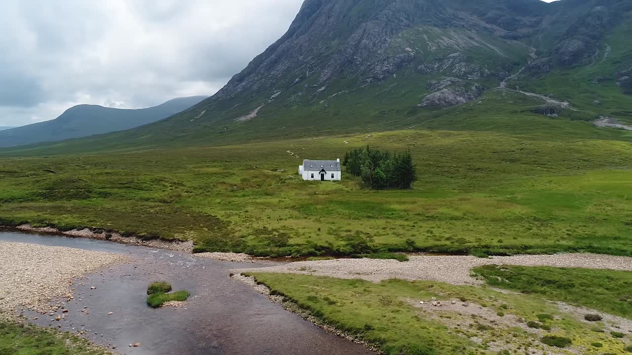 A small cottage in the glencoe valley filmed from above with drone. The lonely house is very close to the river
