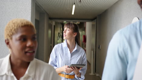 walking in office, woman holding tablet and talking with diverse colleagues