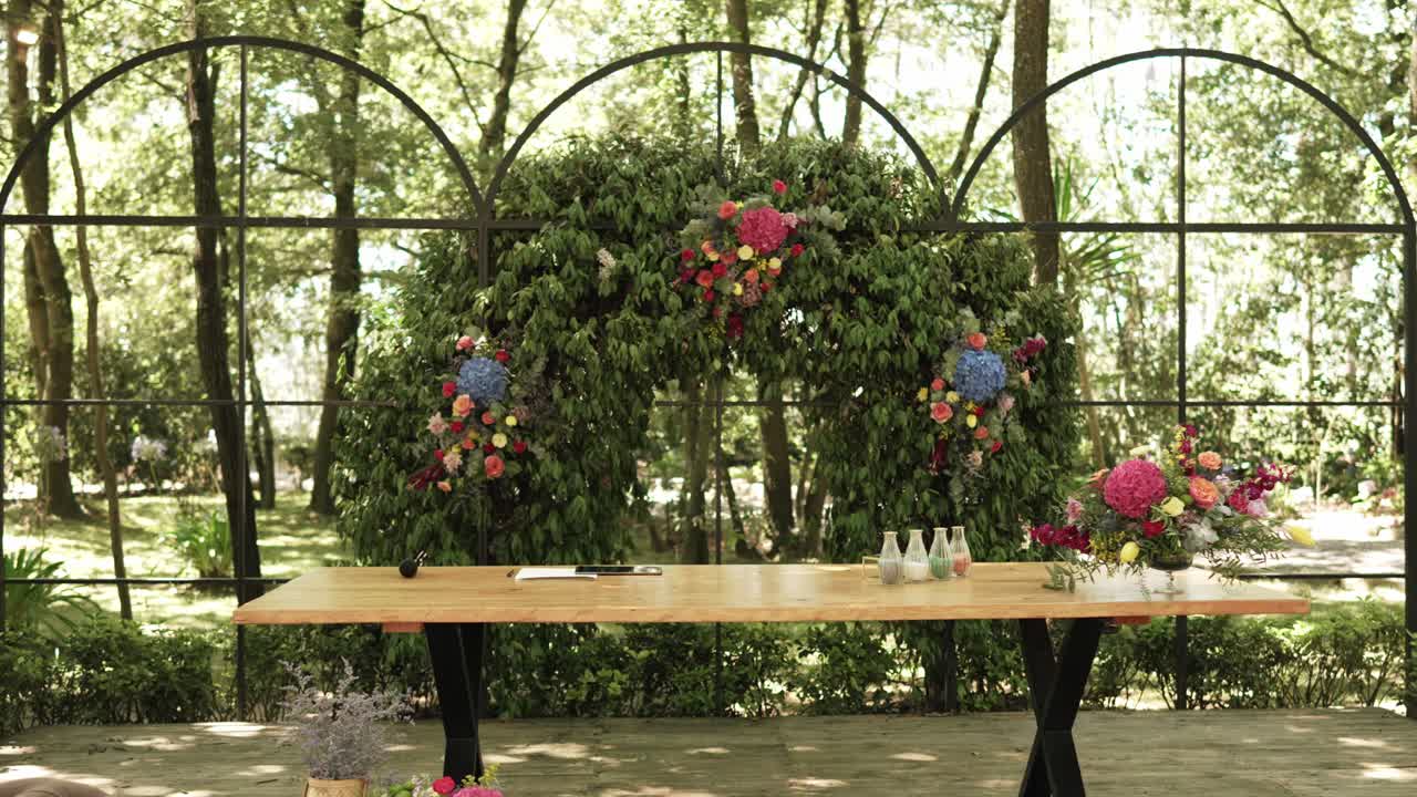 Rustic wedding ceremony setup with a wooden table and a lush floral arch in nature