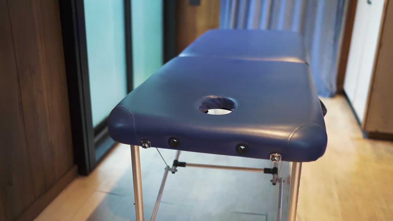 câmera em movimento lento de mesa de massagem em hotel rústico, com paredes de madeira e janela na cena. argentina.