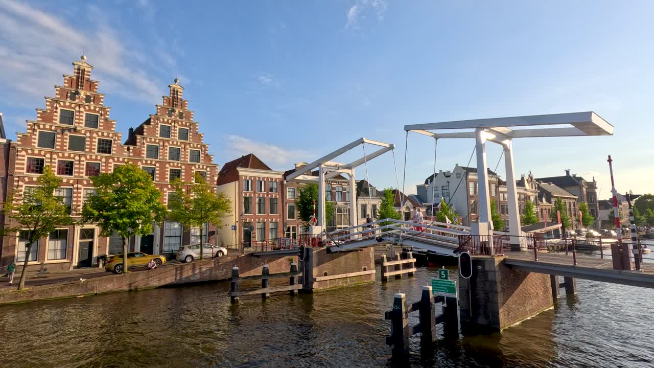 White drawbridge lifts for boat passage, revealing classic Dutch canal houses in golden afternoon light
