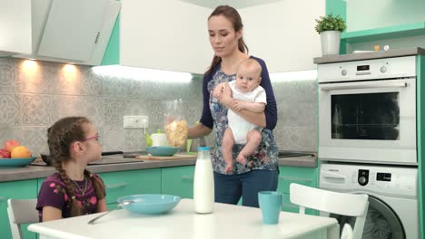 Mother-with-baby-cooking-healthy-breakfast-for-older-daughter
