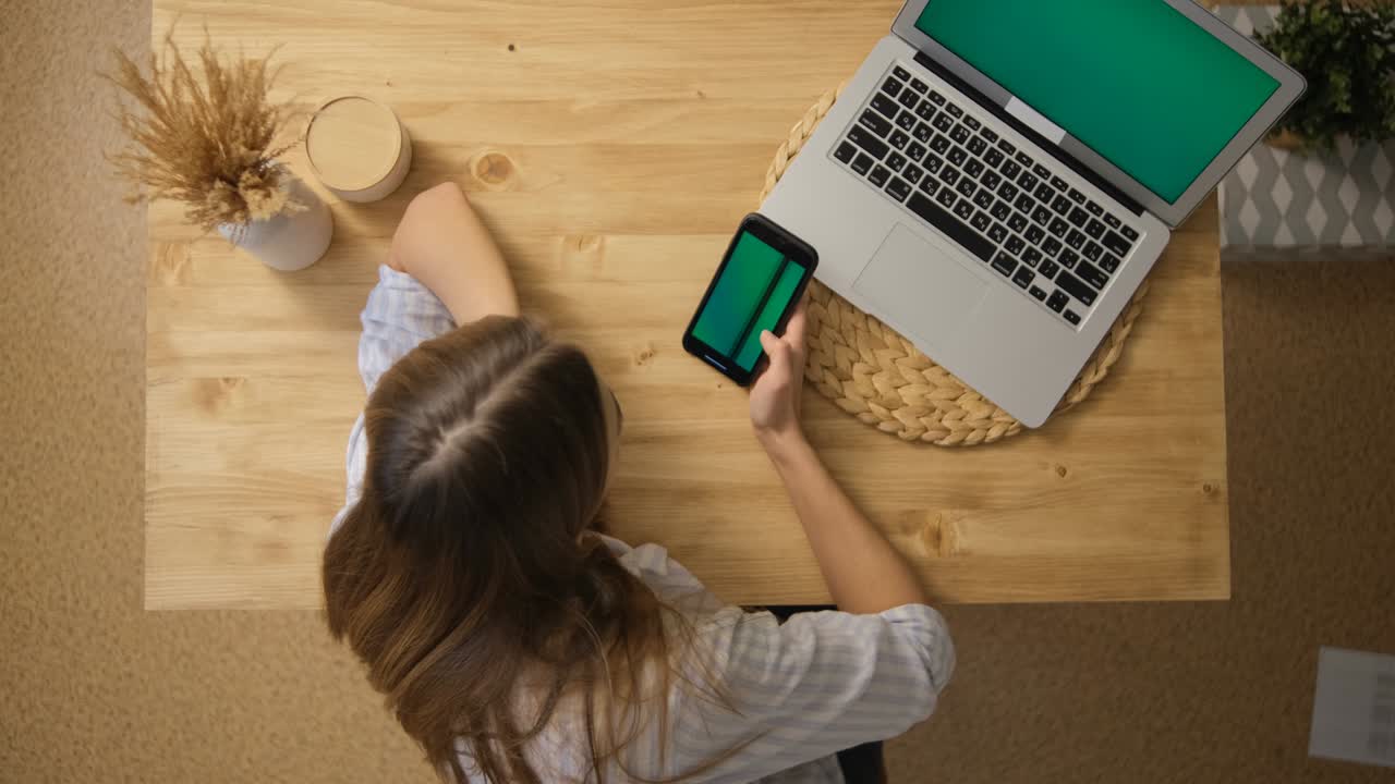A young woman is surfing the Internet through her phone. Green screen. Social network. Top view. Beige colors. The concept of distance education. Green Laptop Monitor.