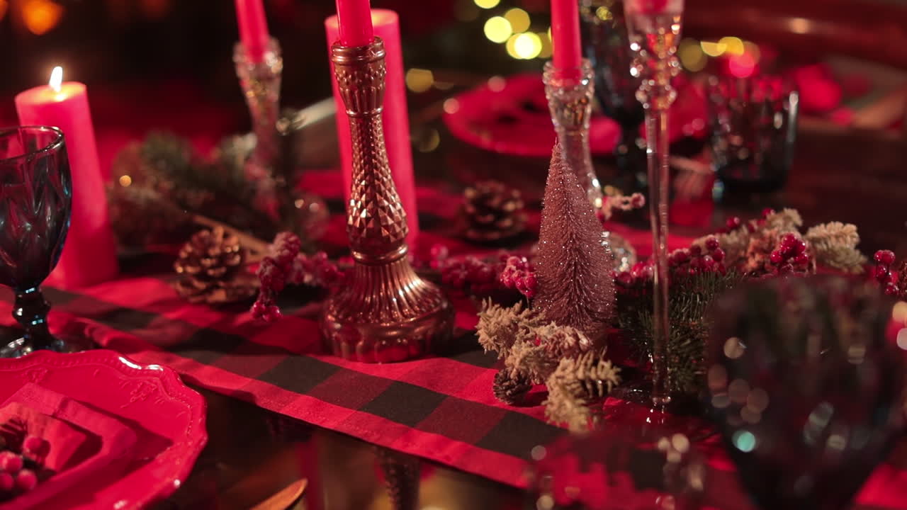 Festively decorated table for Christmas celebration dinner. Red tablecloth, candles, pine cones and glasses on the table. Close up.