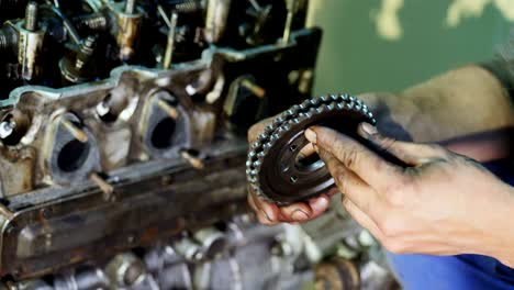 an auto mechanic holds a gearwheel in his hands