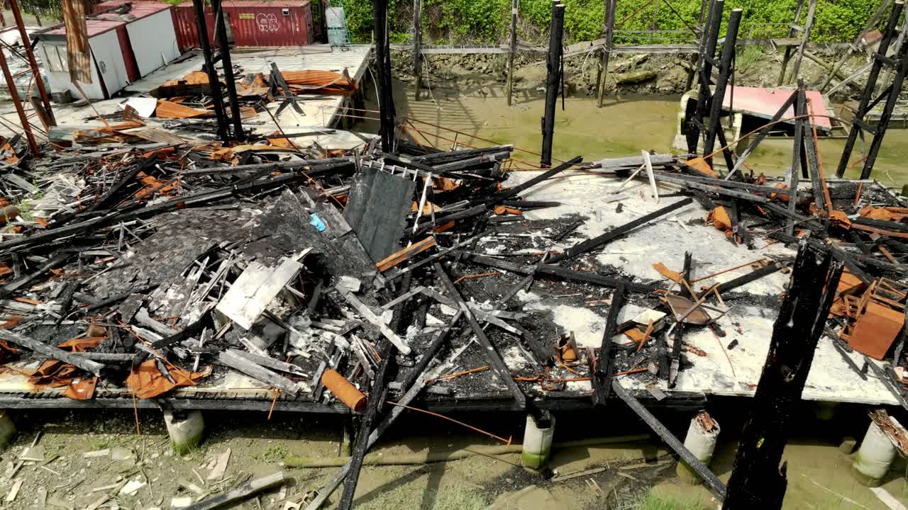 The Charred Ruins of a Riverside Building Lie Next to the Rail Bridge Along River Drive in Richmond, British Columbia, Canada - High Angle Shot