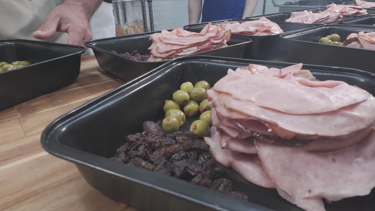 Piatti di prosciutto, olive e uvetta su un tavolo di legno evocano il tema della preparazione dei pasti
