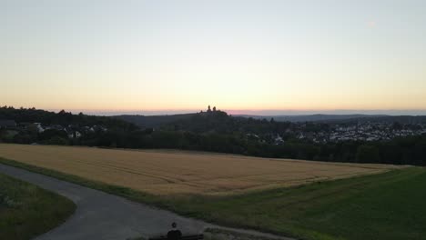 Descending-Aerial-Shot-Of-Braunfels-Castle-With-A-Young-Man-Sitting-On-A-Bench-Admiring-The-Views