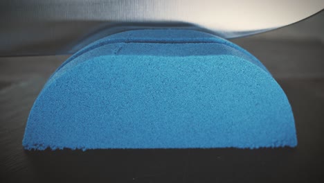 blue kinetic sand is cut with a large knife