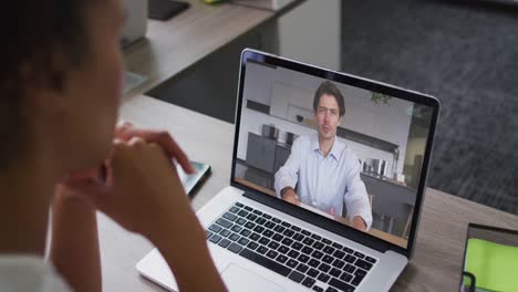 African-american-businesswoman-sitting-at-desk-using-laptop-having-video-call-with-male-colleague