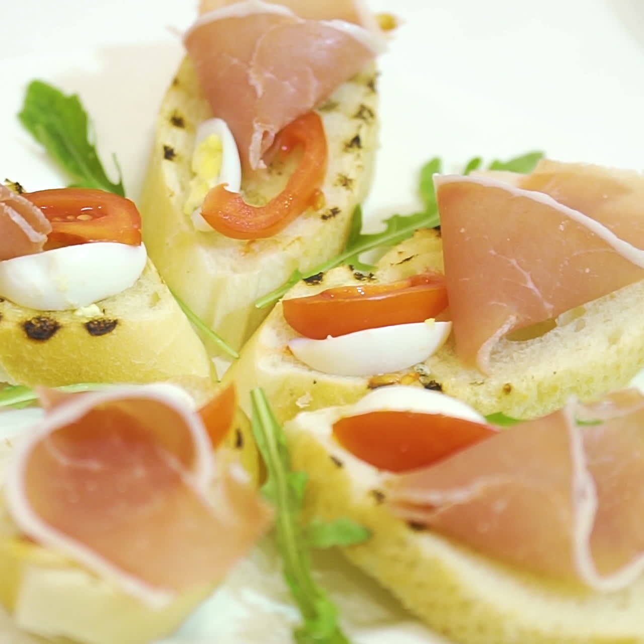A cook decorates a ceramic plate of sandwiches made of cured meat, cherry tomatoes and quail eggs, laying green cilantro leaves between them. Serving of dishes. Close-up.