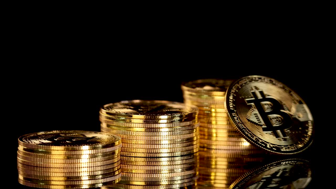 Gold Bitcoin coin rotates and lands upright among stacked coins, dramatic lighting, black background