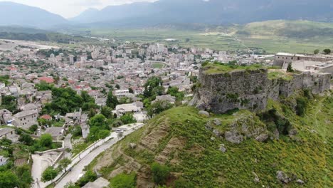 Drone-view-in-Albania-flying-in-Gjirokaster-town-over-a-medieval-castle-on-high-ground-fort-showing-the-brick-brown-roof-houses