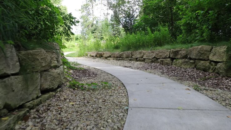 Camera following action of someone walking on the cemented path in the lush green gardens of Paul E
