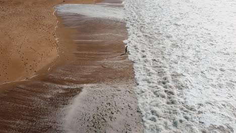 Aerial-view-showing-person-at-shore-of-Atlantic-Iceman-enjoying-foam-of-waves-during-Sunny-day