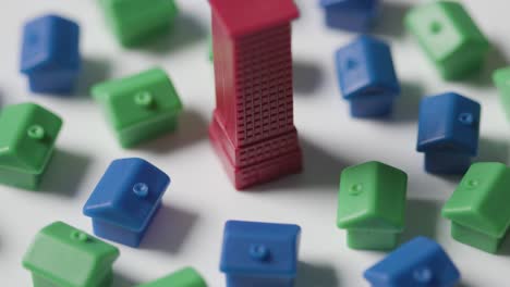 home buying concept with red blue and green plastic models of houses surrounding red skyscraper revolving on white background