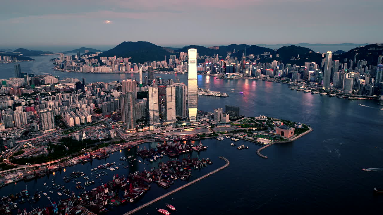 Moon rising above the blinking led lights in the skyline of Hong Kong while boats travel over Victoria harbour