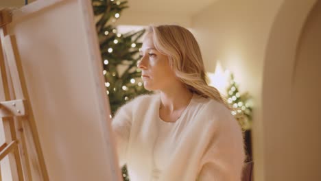 stunning blonde girl painting on canvas in cozy and warm room