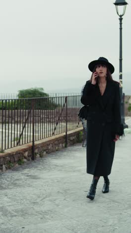 elegant woman in total black walking with the phone in the town park
