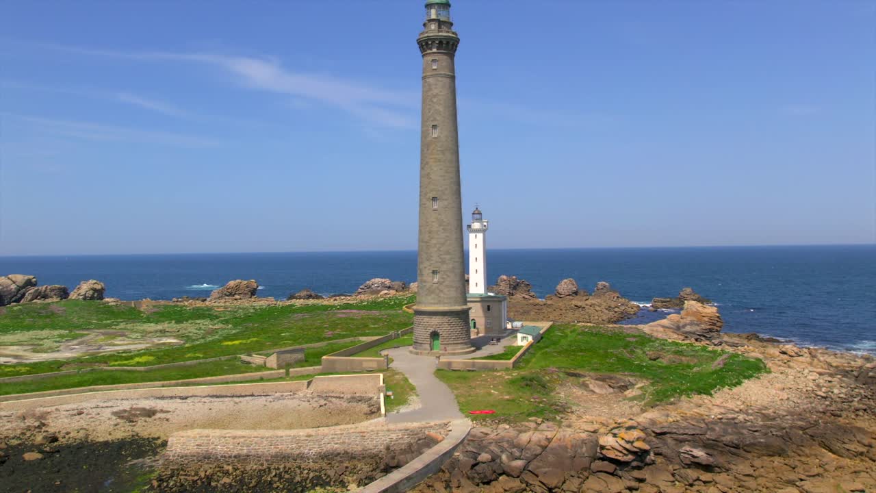 A close-up drone shot of the iconic Phare de l’Île Vierge lighthouse in Plouguerneau, Brittany, France, highlighting its rocky coastal landscape and surrounding deep blue waters of the Atlantic Ocean.