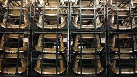 handheld camera capturing a sea of metal parts, neatly stacked on mobile black racks in a warehouse, under the artificial glow of overhead fluorescent lights