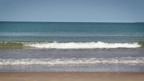 olas de agua clara rompen y ruedan hacia una playa de arena