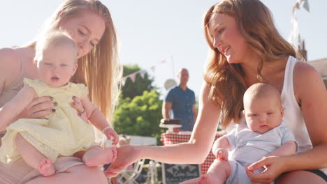 Zeitlupenaufnahme-Von-Zwei-Müttern,-Die-Auf-Einem-Teppich-Sitzen-Und-Mit-Babys-Beim-Sommergartenfest-Spielen