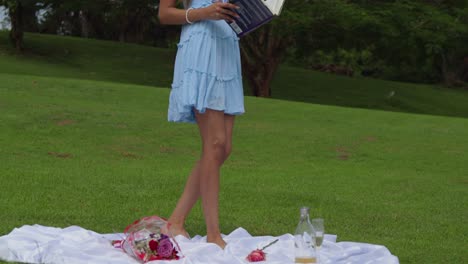 a young woman walking wwhile opening her book in a park picnic setting