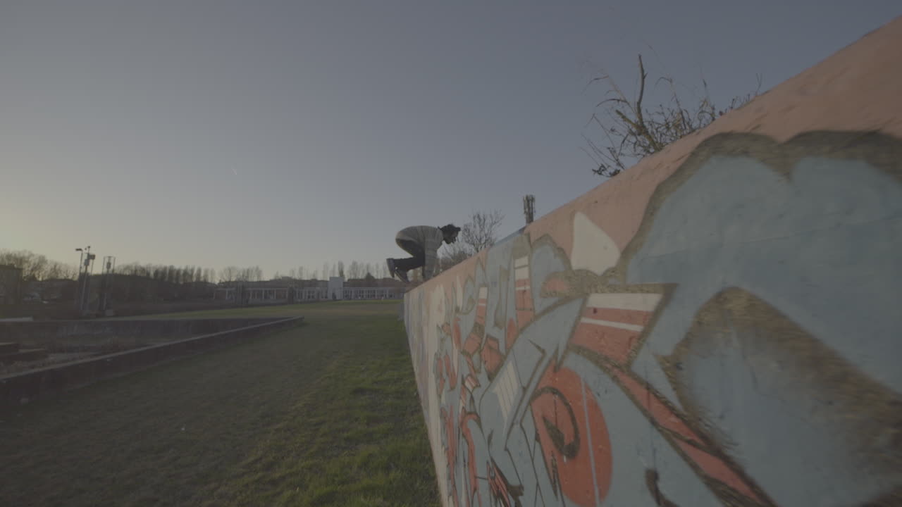 Parkour and skateboarding stunts on a graffiti wall during sunset