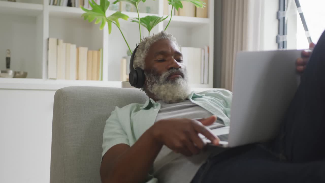 Video of african american senior man using laptop and headphones