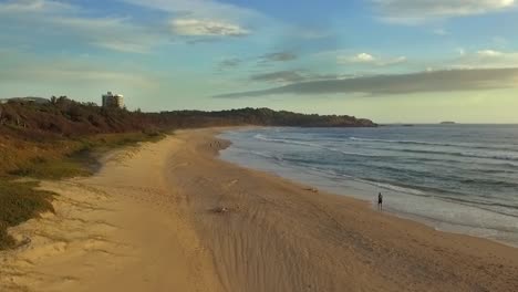 toma aérea de drones viajando de un corredor corriendo por la playa en el puerto de coffs