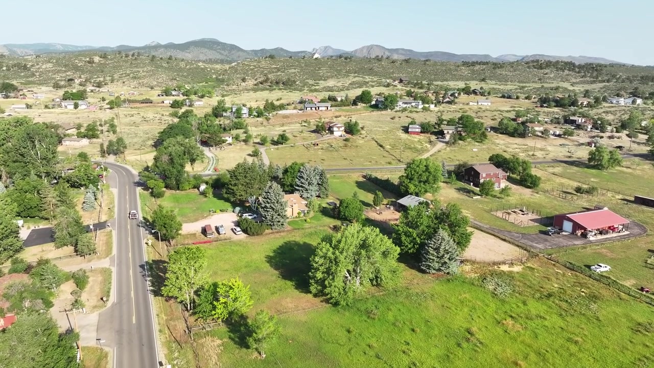 Scatto panoramico ad alta quota che mostra case in stile ranch, fienili e strade sterrate che costeggiano le colline pedemontane della catena montuosa anteriore.