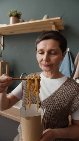 woman eating noodles from a takeout box with chopsticks