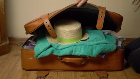 femme fermant la valise avec un chapeau de paille et des vêtements plan large