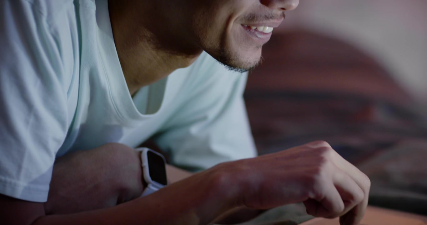 Seeing laptop message, African American man smiling, leaning in bed, tapping trackpad checking text