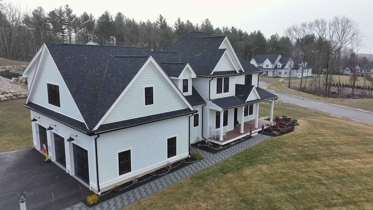White villa with black roof in suburb neighborhood of America. Snowy winter day with flying flurries. Aerial approaching shot.