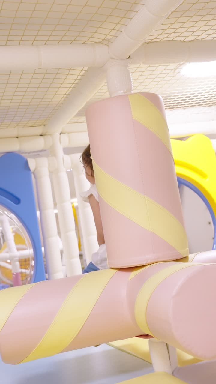 A gorgeous 5-year-old girl smiles brightly as she spins around on a colorful marshmallow-themed soft play structure at an indoor playground