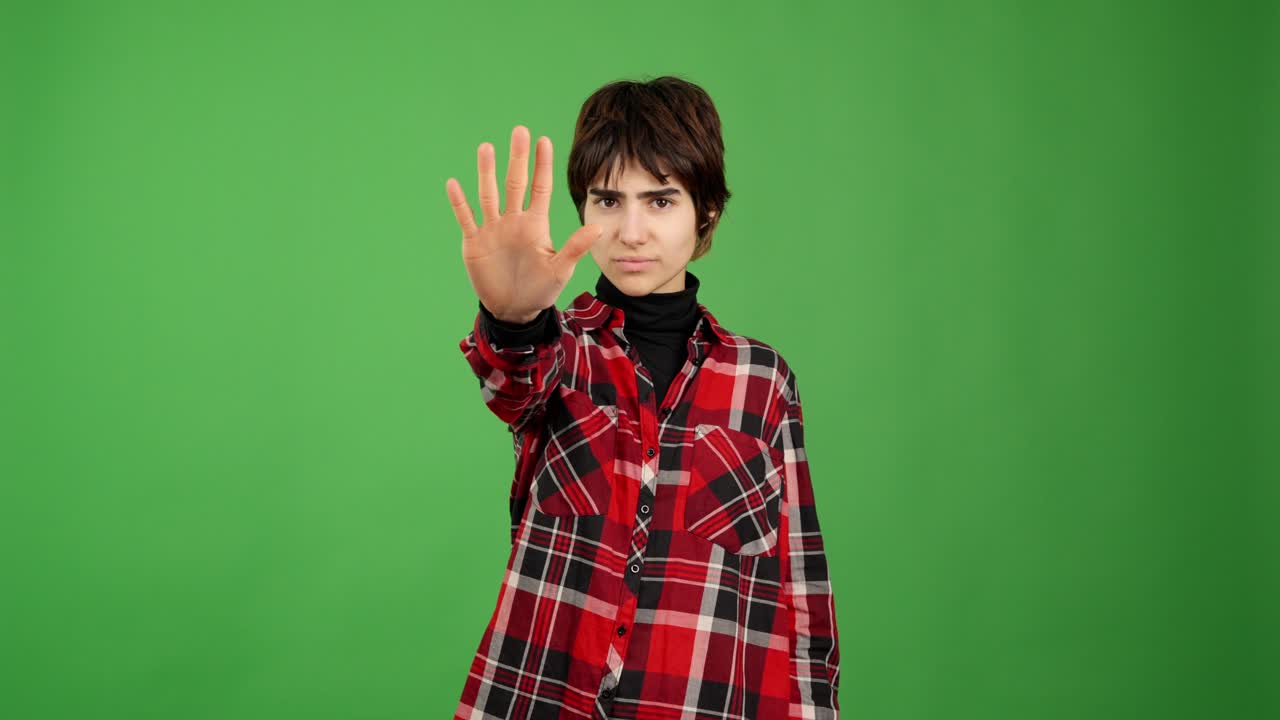 Giovane che fa un gesto di stop con la mano su sfondo verde
